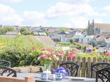 A patio table set with a blue teapot two mugs sugar bowl and flowers with a town and church in the background at Crab Pot Cottage in Porthleven