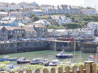 A small harbor with boats docked in the water and stone buildings along the waterfront at Crab Pot Cottage in Porthleven