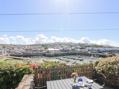 A patio table with chairs overlooking a harbor with boats and houses at Crab Pot Cottage in Porthleven