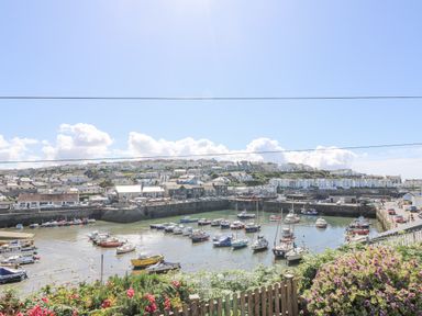 A harbor with boats docked and houses on a hill in the background at Crab Pot Cottage in Porthleven