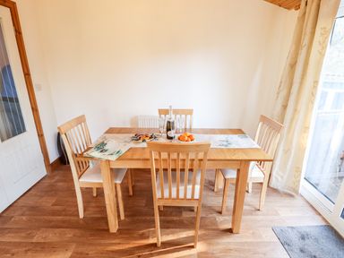 A dining area with a wooden table four chairs a table runner a bottle with glasses and a bowl of oranges at Kantankye Lodge Thorpe St Peter near Wainfleet All Saints