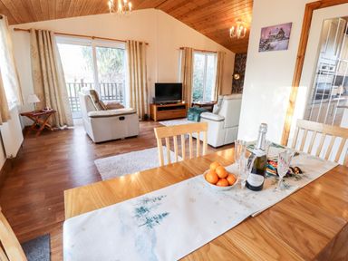 A dining table with a bottle and glasses near a living room with sofas and a television at Kantankye Lodge in Thorpe St Peter near Wainfleet All Saints