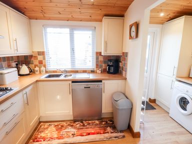 A kitchen with a sink under window white cabinets dishwasher washing machine and tiled backsplash at Kantankye Lodge Thorpe St Peter near Wainfleet All Saints