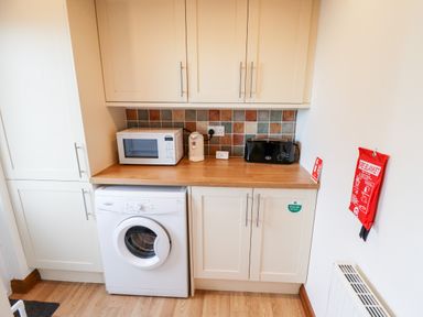 A kitchen area with a microwave kettle toaster washing machine and cabinets at Kantankye Lodge Thorpe St Peter near Wainfleet All Saints