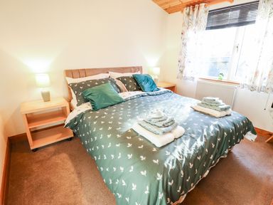 A bedroom with a double bed dressed in patterned bedding and two bedside tables with lamps at Kantankye Lodge Thorpe St Peter near Wainfleet All Saints
