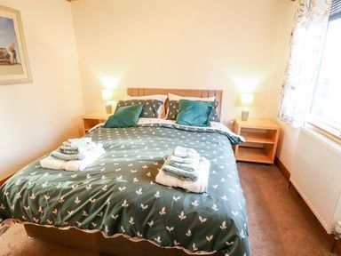 A bedroom with a double bed with green patterned bedding and towels on top two bedside tables with lamps a window with patterned curtains and a radiator Kantankye Lodge Thorpe St Peter near Wainfleet All Saints