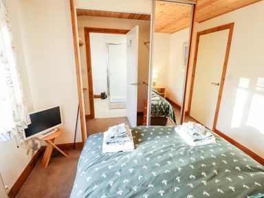 A bedroom with a bed covered in green patterned bedding a small TV on a wooden stand and a mirrored wardrobe showing a bathroom at Kantankye Lodge Thorpe St Peter near Wainfleet All Saints