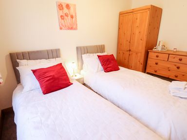 A bedroom with two single beds with red pillows a wooden wardrobe and dresser at Kantankye Lodge Thorpe St Peter near Wainfleet All Saints