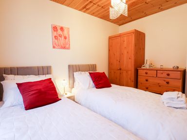 A bedroom with two single beds white bedding red pillows a wooden wardrobe and dresser at Kantankye Lodge Thorpe St Peter near Wainfleet All Saints