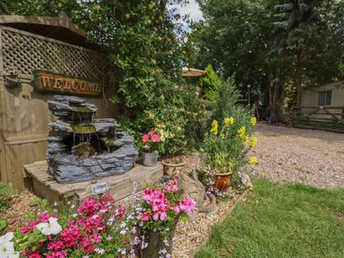 A garden with a stone water fountain flowers and plants near a wooden fence at Kantankye Lodge Thorpe St Peter near Wainfleet All Saints