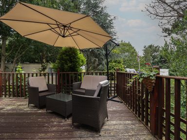 A wooden deck with outdoor furniture and a large umbrella surrounded by trees at Kantankye Lodge Thorpe St Peter near Wainfleet All Saints