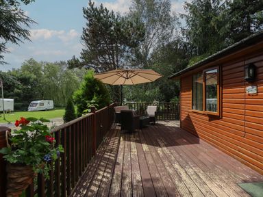 A wooden deck with outdoor chairs and table under an umbrella at Kantankye Lodge in Thorpe St Peter near Wainfleet All Saints