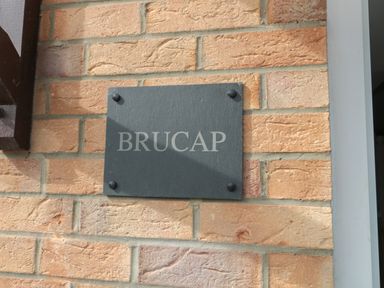 A black rectangular plaque with the word BRUCAP mounted on a brick wall at Brucap Cottage in Beadnell