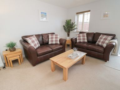 A living room with two brown leather sofas with plaid cushions a wooden coffee table and side tables with plants at Brucap Cottage in Beadnell