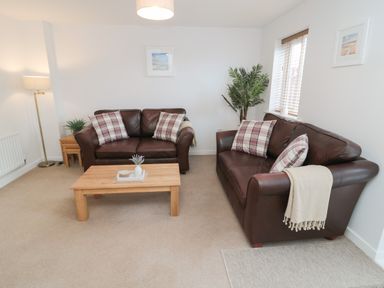 A living room with two brown leather sofas a wooden coffee table and a floor lamp at Brucap Cottage in Beadnell