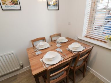 A dining table set for four with white dishes and glasses by a window with wooden blinds at Brucap Cottage in Beadnell