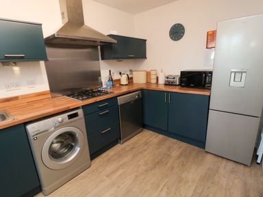 A kitchen with washing machine dishwasher microwave toaster refrigerator and blue cabinets at Brucap Cottage in Beadnell
