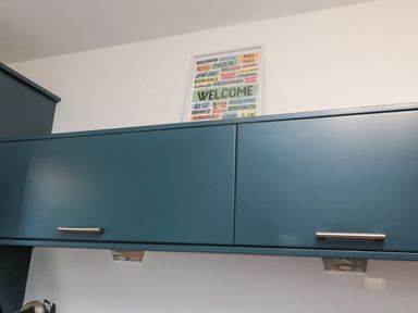 A kitchen with blue cabinets and a framed welcome sign on the wall at Brucap Cottage in Beadnell