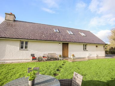 A backyard with outdoor seating and a table with a plant next to a house with a tiled roof at Rhyd Y Bont Bach in Rhoscolyn