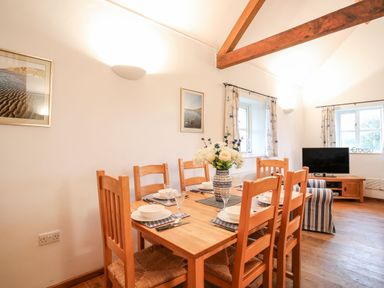 A dining area with a wooden table set for six and a living space with a TV and striped armchair at Rhyd Y Bont Bach in Rhoscolyn