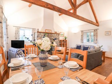 A dining table with place settings and a vase of flowers in a living room with sofas stone fireplace and wooden beams at Rhyd Y Bont Bach in Rhoscolyn