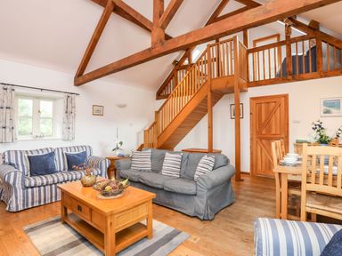 A living room with wooden ceiling beams sofas coffee table dining table and staircase at Rhyd Y Bont Bach in Rhoscolyn