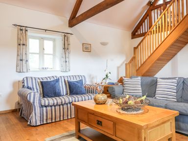 A living room with striped sofas wooden coffee table and staircase at Rhyd Y Bont Bach in Rhoscolyn