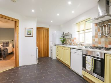 A kitchen with yellow cabinets a gas stove dishwasher washing machine and a window at Rhyd Y Bont Bach in Rhoscolyn