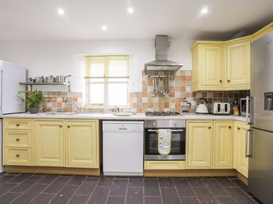 A kitchen with yellow cabinets white dishwasher oven stove and stainless steel refrigerator at Rhyd Y Bont Bach in Rhoscolyn
