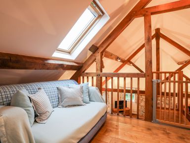 A loft area with a sofa under a skylight and wooden beams at Rhyd Y Bont Bach in Rhoscolyn