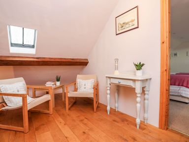 A sitting area with two wooden armchairs and a small table between them a white console table with plants and a framed picture on the wall at Rhyd Y Bont Bach in Rhoscolyn