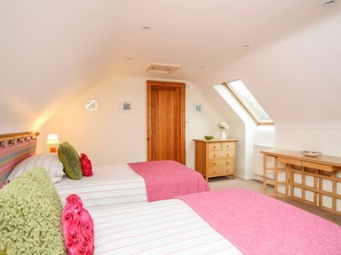 A bedroom with two single beds a small wooden dresser and a wooden desk under a slanted ceiling at Rhyd Y Bont Bach in Rhoscolyn