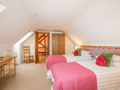 A bedroom with two single beds with striped bedding and pink blankets a wooden wardrobe a wooden chair a wooden desk and an open door at Rhyd Y Bont Bach in Rhoscolyn