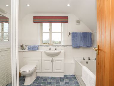 A bathroom with a toilet sink bathtub blue towels and a window at Rhyd Y Bont Bach in Rhoscolyn