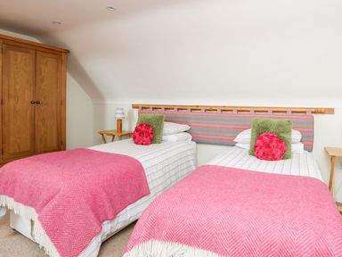 A bedroom with two single beds with pink blankets and decorative pillows a wooden wardrobe and bedside tables at Rhyd Y Bont Bach in Rhoscolyn