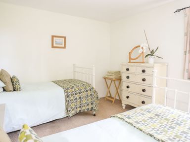 A bedroom with two single beds a white chest of drawers with a mirror and a potted plant folded towels on a wooden stand and a framed picture on the wall at Rhyd Y Bont Bach in Rhoscolyn