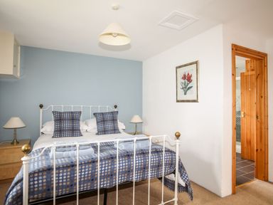 A bedroom with a metal bed frame blue patterned bedding two bedside tables with lamps and a framed flower picture on the wall at Rhyd Y Bont Bach in Rhoscolyn