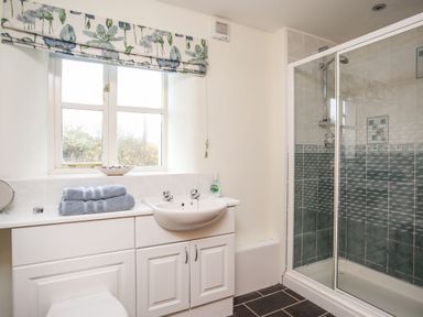 A bathroom with a sink and folded towels on a cabinet next to a shower enclosure with tiled walls at Rhyd Y Bont Bach in Rhoscolyn