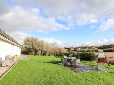 A backyard with outdoor chairs a table and a barbecue grill at Rhyd Y Bont Bach in Rhoscolyn