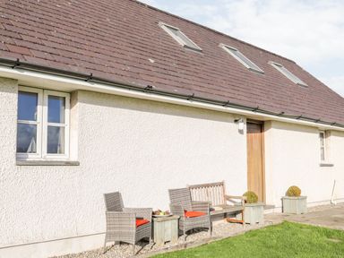 Exterior of a building with two windows a wooden door three skylights two chairs a wooden bench and potted plants at Rhyd Y Bont Bach in Rhoscolyn