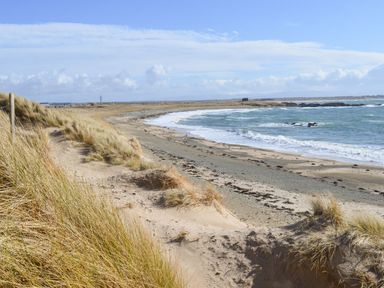 A sandy beach with grassy dunes and waves at Rhyd Y Bont Bach in Rhoscolyn