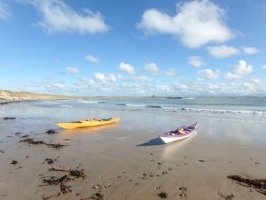 Two kayaks on a sandy beach with seaweed and waves under a blue sky with clouds at Rhyd Y Bont Bach in Rhoscolyn
