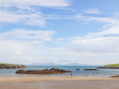 A sandy beach with rocky outcrops and people near the water at Rhyd Y Bont Bach in Rhoscolyn