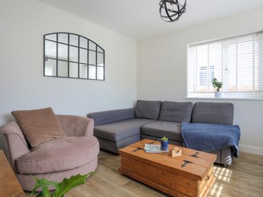 A living room with a round armchair gray sectional sofa wooden coffee table and window with blinds at Iscoed Llangefni