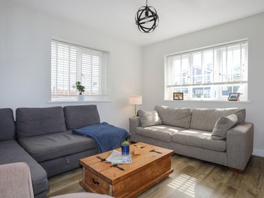 A living room with two sofas a wooden coffee table a lamp and windows with blinds at Iscoed in Llangefni