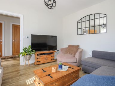 A living room with a large television on a wooden cabinet and a round chair at Iscoed in Llangefni