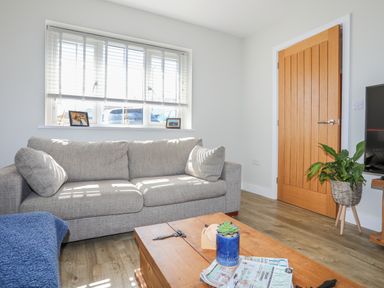 A living room with a gray sofa wooden door and coffee table with magazines and plant at Iscoed in Llangefni
