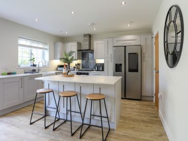 A kitchen with an island and three stools a refrigerator and a round wall mirror at Iscoed in Llangefni