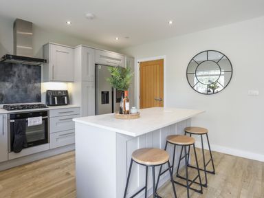 A kitchen with an island and three stools a refrigerator stove and round wall mirror at Iscoed in Llangefni