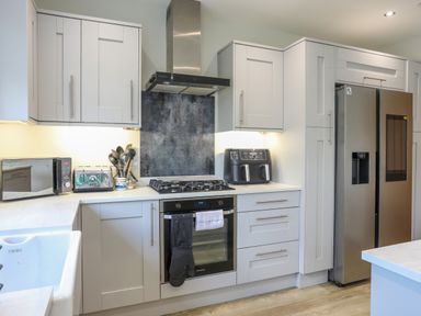 A kitchen with white cabinets a stainless steel refrigerator an oven a gas stove a microwave a toaster and kitchen utensils at Iscoed in Llangefni
